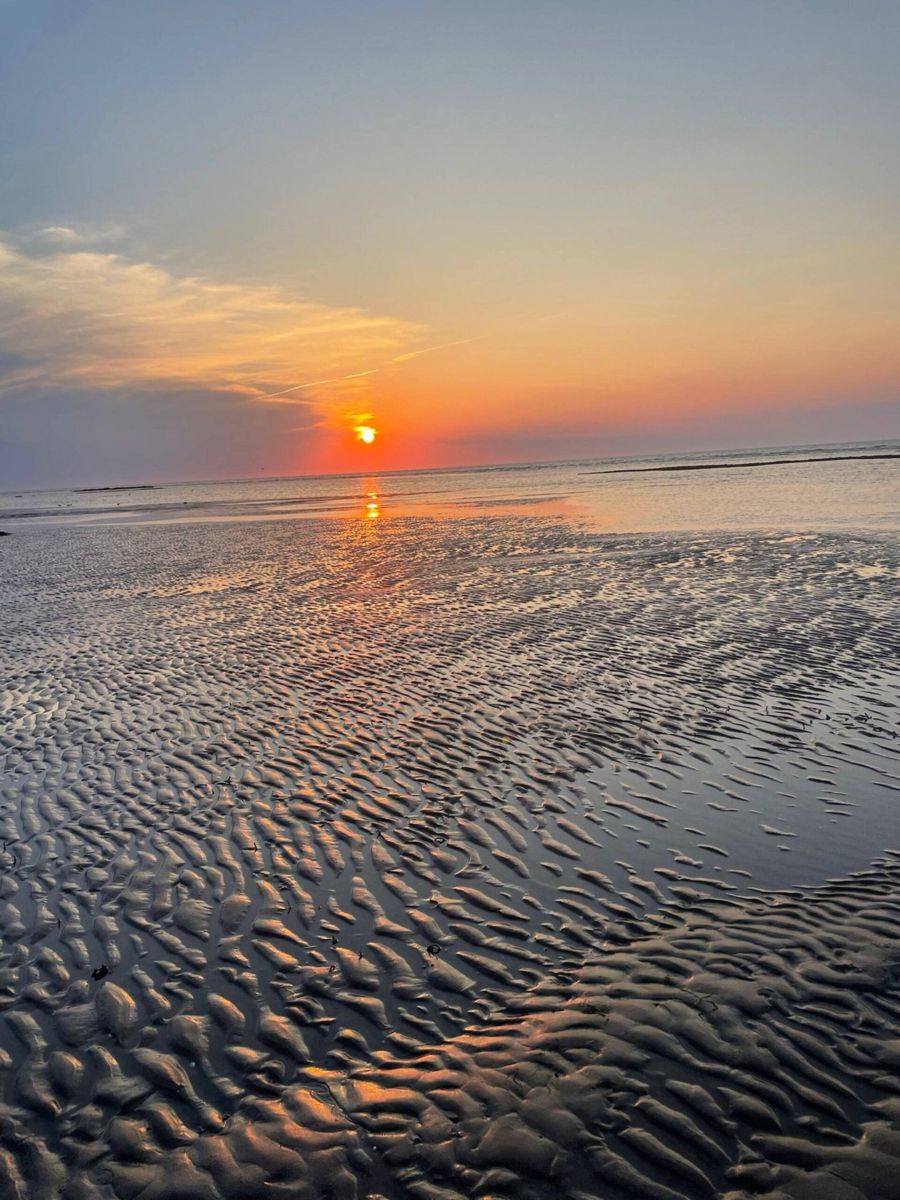The sun setting low over wet rippled sand, with an orange sky reflected in the pools