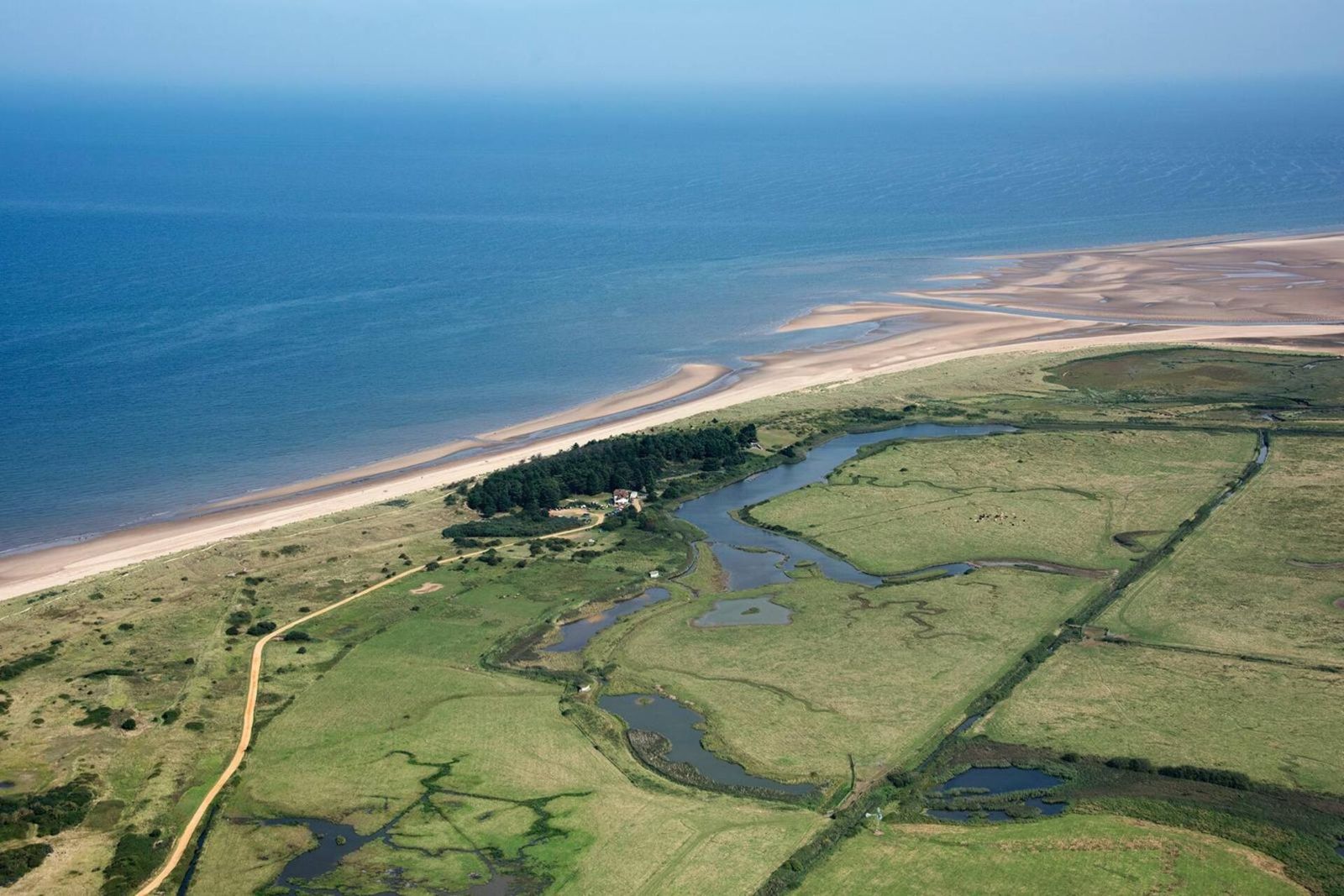 An aerial view of green saltmarsh and creeks behind a long strip of sand and the sea