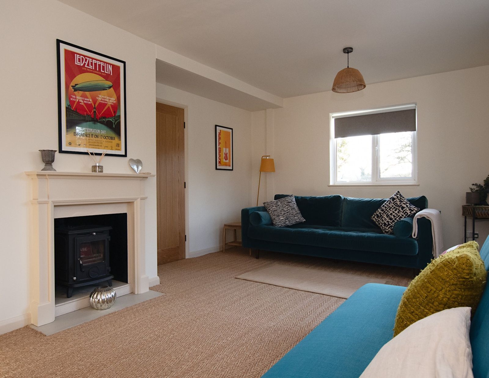 A living room with a white fireplace, a teal sofa, a pendant light and a bright framed poster above the mantelpiece