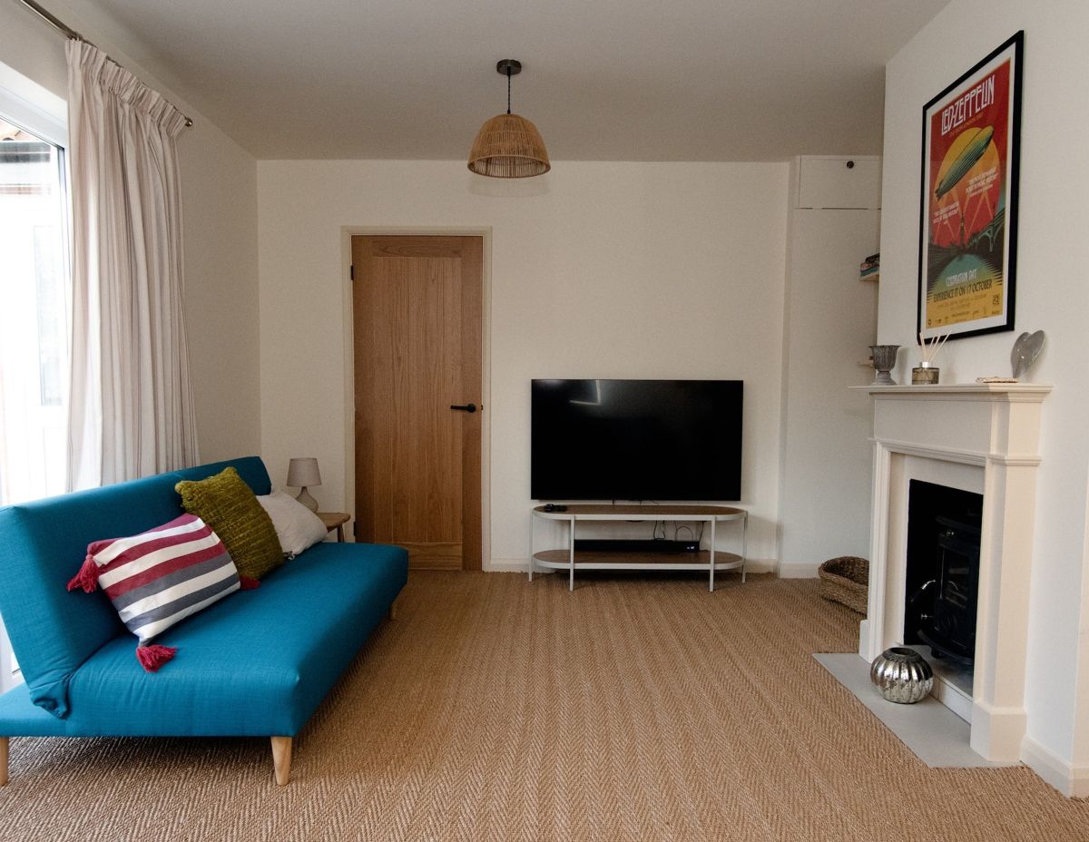 A living room with a teal sofa bed, striped cushions, a television on a white stand and a fireplace