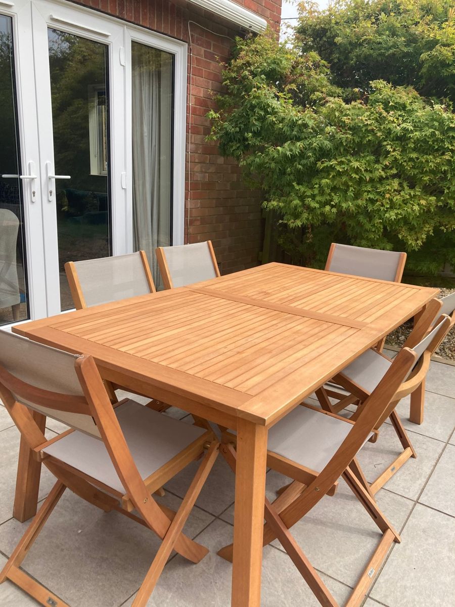 A wooden outdoor dining table and chairs on a pale stone patio beside French doors